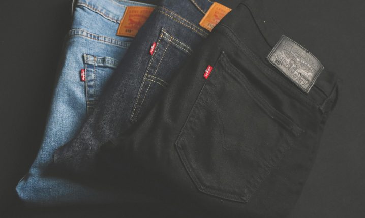 A stack of blue, dark, and black denim jeans folded on a dark surface.